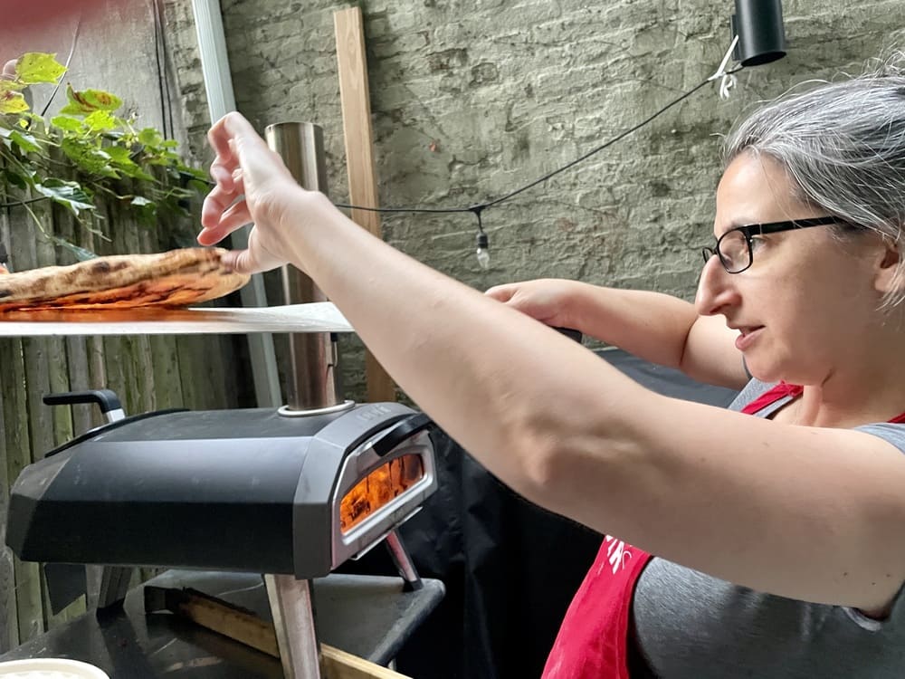 woman holding up a pizza and looking under it